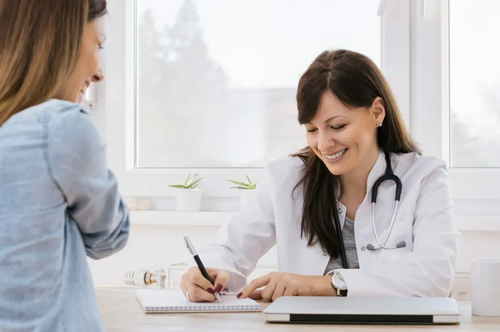 Eine freundliche Ärztin notiert eine Diagnose, während ihre Patientin ihr gegenüber sitzt.