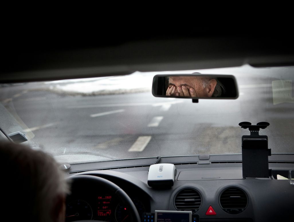 Ausschnitt einer Windschutzscheibe im Auto – im Rückspiegel ist ein Mann mit Brille am Steuer zu sehen, der sich die Augen reibt.