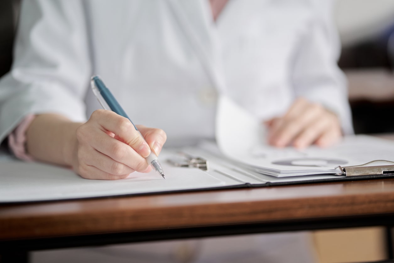 Der Oberkörper einer Ärztin, die an einem Tisch sitzt und etwas notiert.