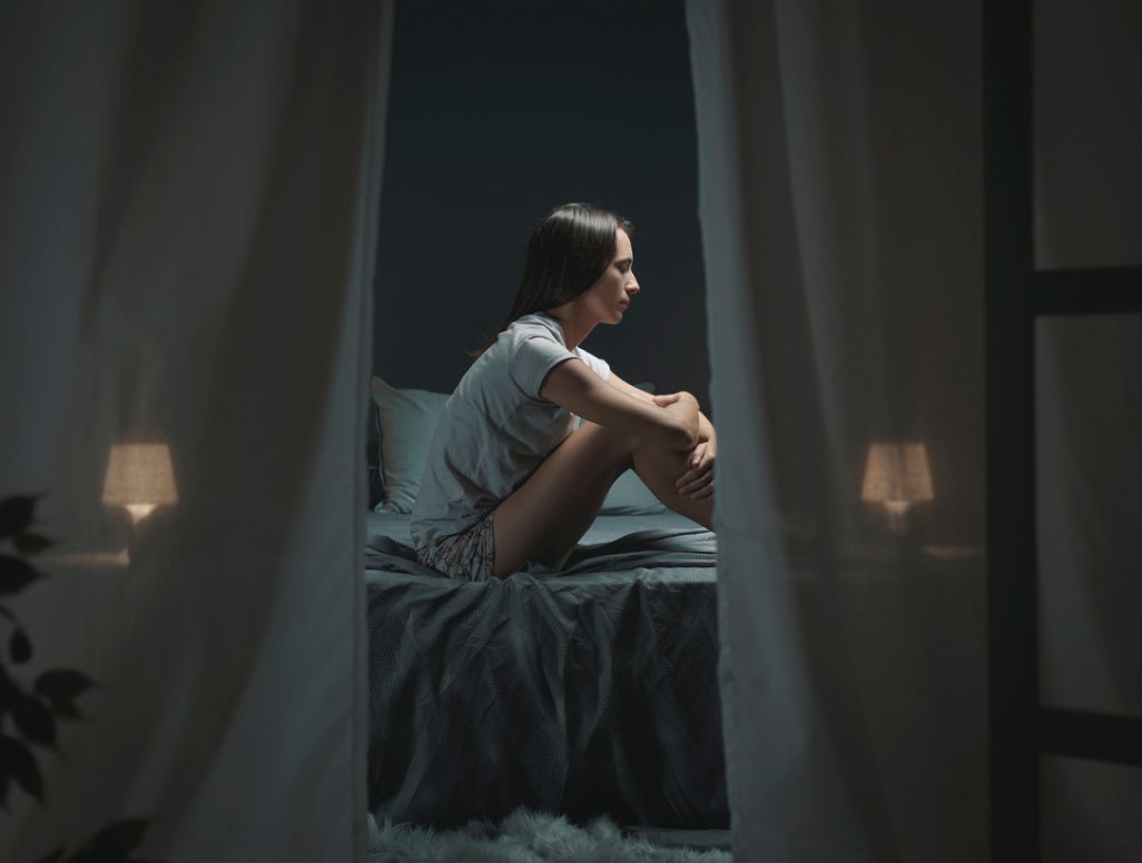 Frau sitzt auf dem Bett und kann nicht schlafen, weil es zu heiß ist